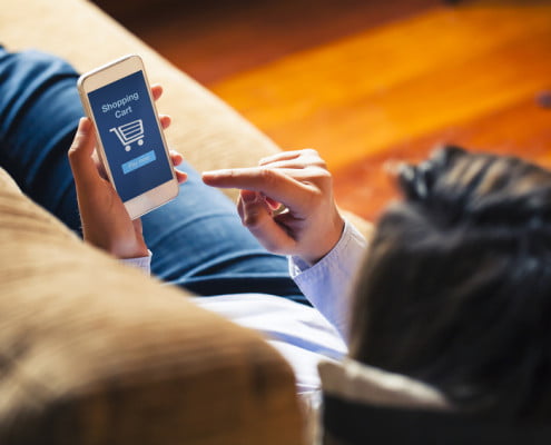 Woman shopping by mobile phone laying at home. Blue screen. She is laying on the sofa.