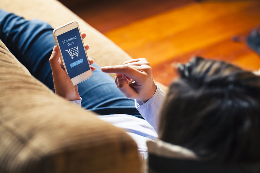 Woman shopping by mobile phone laying at home. Blue screen. She is laying on the sofa.